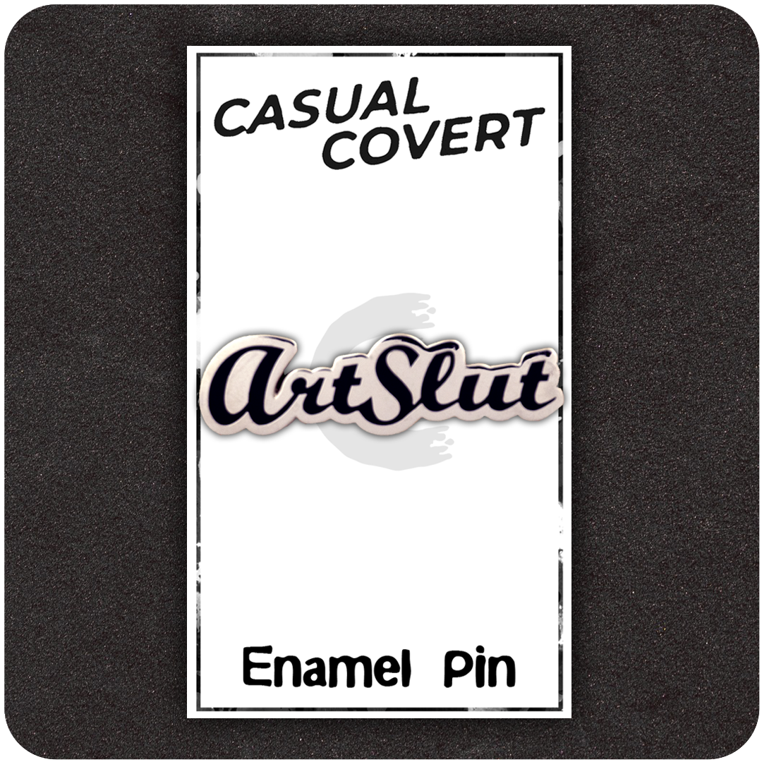 ArtSlut enamel pin on branded Casual Covert backing card with bold cursive lettering in black and white, displayed on a dark foam background.