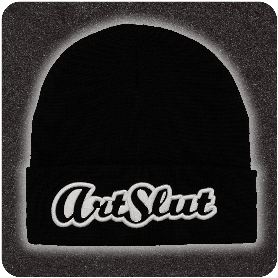 Black knit beanie featuring bold white embroidered βArt Slutβ text on the front fold, displayed on a textured dark background with soft gradient lighting.