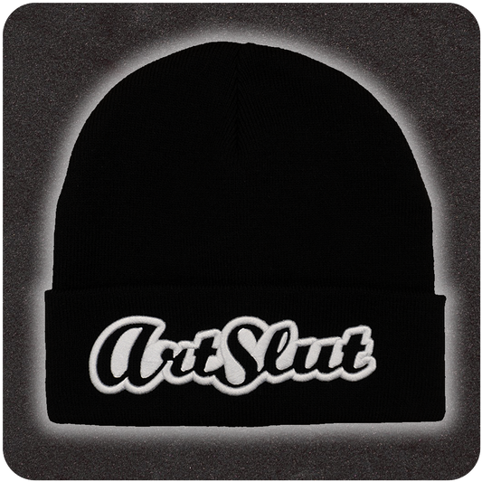 Black knit beanie featuring bold white embroidered βArt Slutβ text on the front fold, displayed on a textured dark background with soft gradient lighting.
