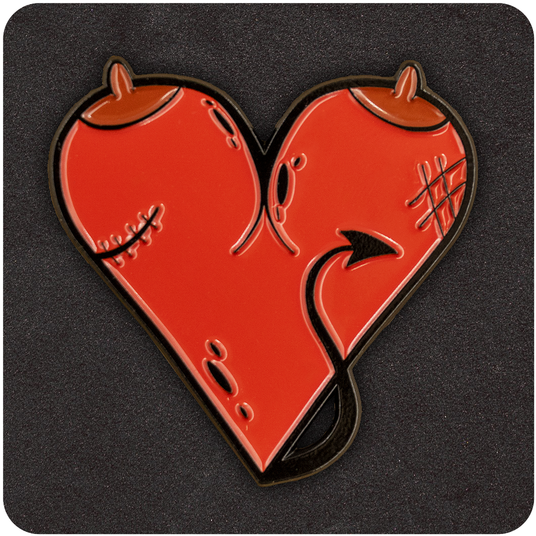 Red heart-shaped enamel pin featuring devilish details including horns, a tail, stitches, and textured scars, displayed on a dark background.