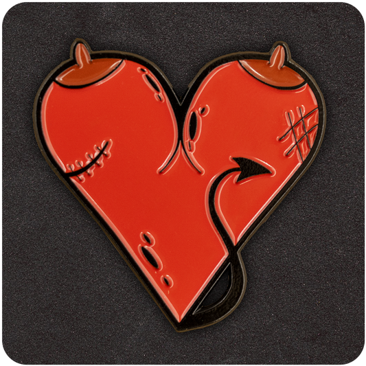 Red heart-shaped enamel pin featuring devilish details including horns, a tail, stitches, and textured scars, displayed on a dark background.