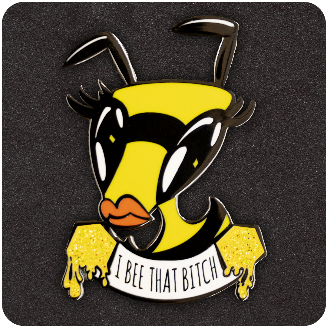 Sassy enamel pin featuring a fierce cartoon bee with bold eyelashes, orange lips, and a dripping honey banner that reads “I Bee That Bitch.” Set against a dark foam background.