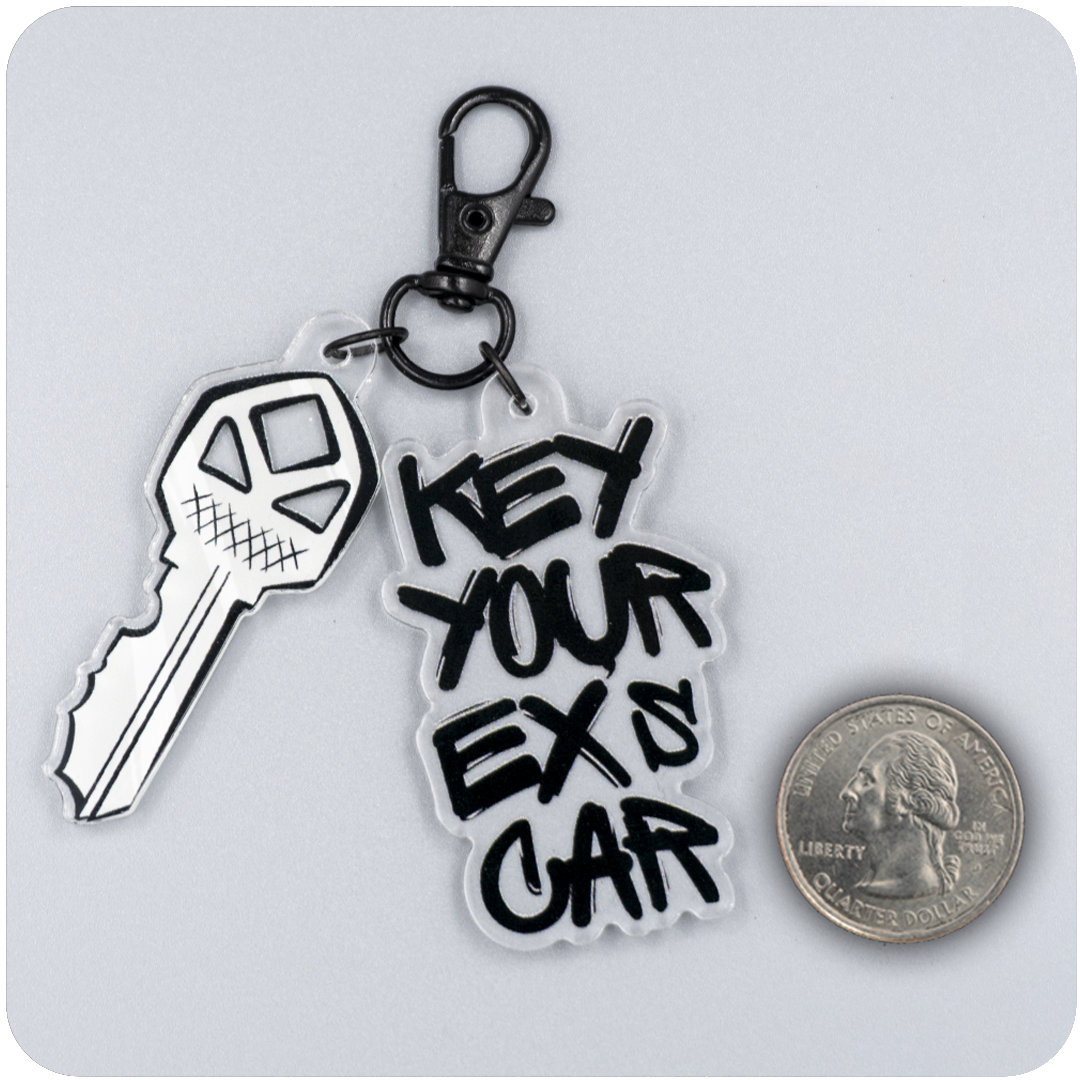 Acrylic keychain with a cartoon-style jagged key and bold black graffiti text reading “Key Your Ex’s Car,” attached to a black lobster clasp. A U.S. quarter is placed beside it on a gray background to show scale.