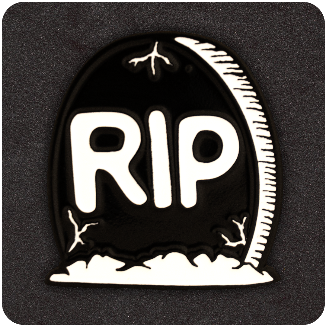 Black and white enamel pin shaped like a tombstone with bold “RIP” lettering and cracked detailing, displayed on a dark textured background.