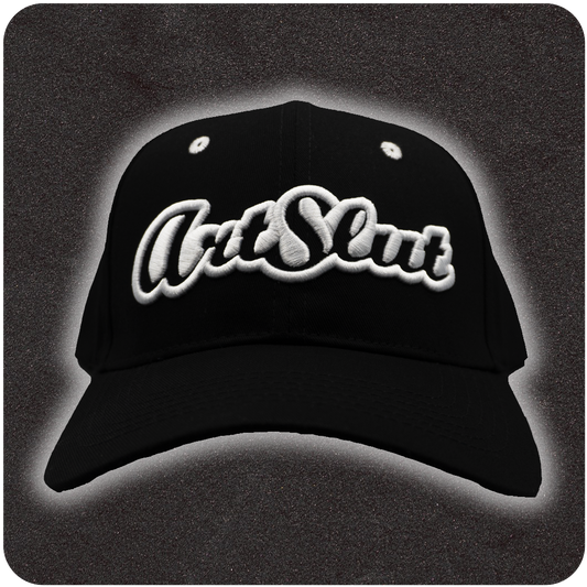 Front view of a black snapback hat with bold white embroidered βArt Slutβ logo, centered on a structured crown and displayed against a dark textured backdrop with soft halo lighting.