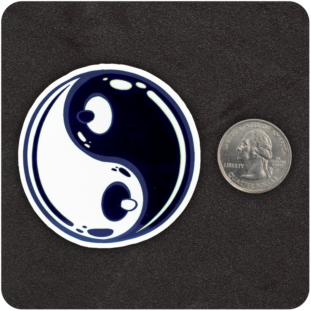 A circular sticker featuring a glossy, stylized yin-yang design with a playful twist—each of the inner dots is shaped like a cartoon nipple, giving the symbol a cheeky, breast-like appearance. The sticker is placed on a black textured background next to a U.S. quarter for scale.