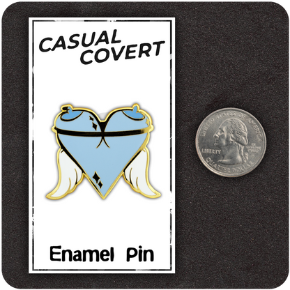 Angel Tits enamel pin displayed on Casual Covert card with a U.S. quarter for scale, featuring a heart-shaped design made from cartoon angelic breasts with halos and white wings outlined in gold.