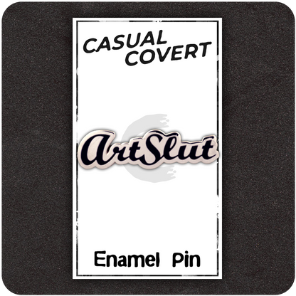 ArtSlut enamel pin on branded Casual Covert backing card with bold cursive lettering in black and white, displayed on a dark foam background.