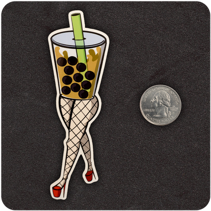 A vinyl sticker featuring a stylized cup of boba tea with a green straw and large black tapioca pearls. The cup is personified with shapely legs in fishnet stockings and red high heels, posed flirtatiously. A U.S. quarter is placed next to the sticker for size comparison, all on a dark textured background.