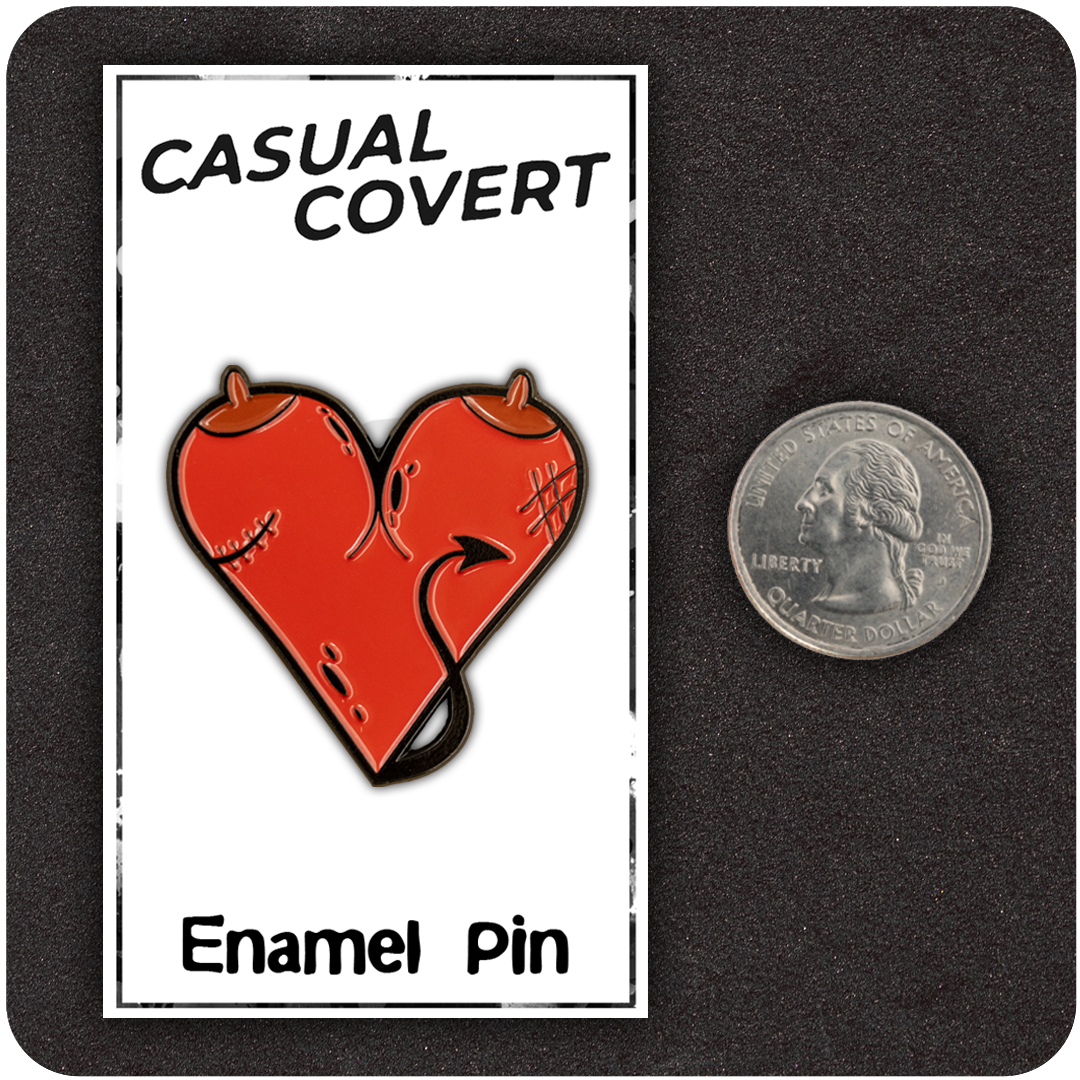 The Casual Covert Demon Tits Enamel Pin next to a quarter for scale.