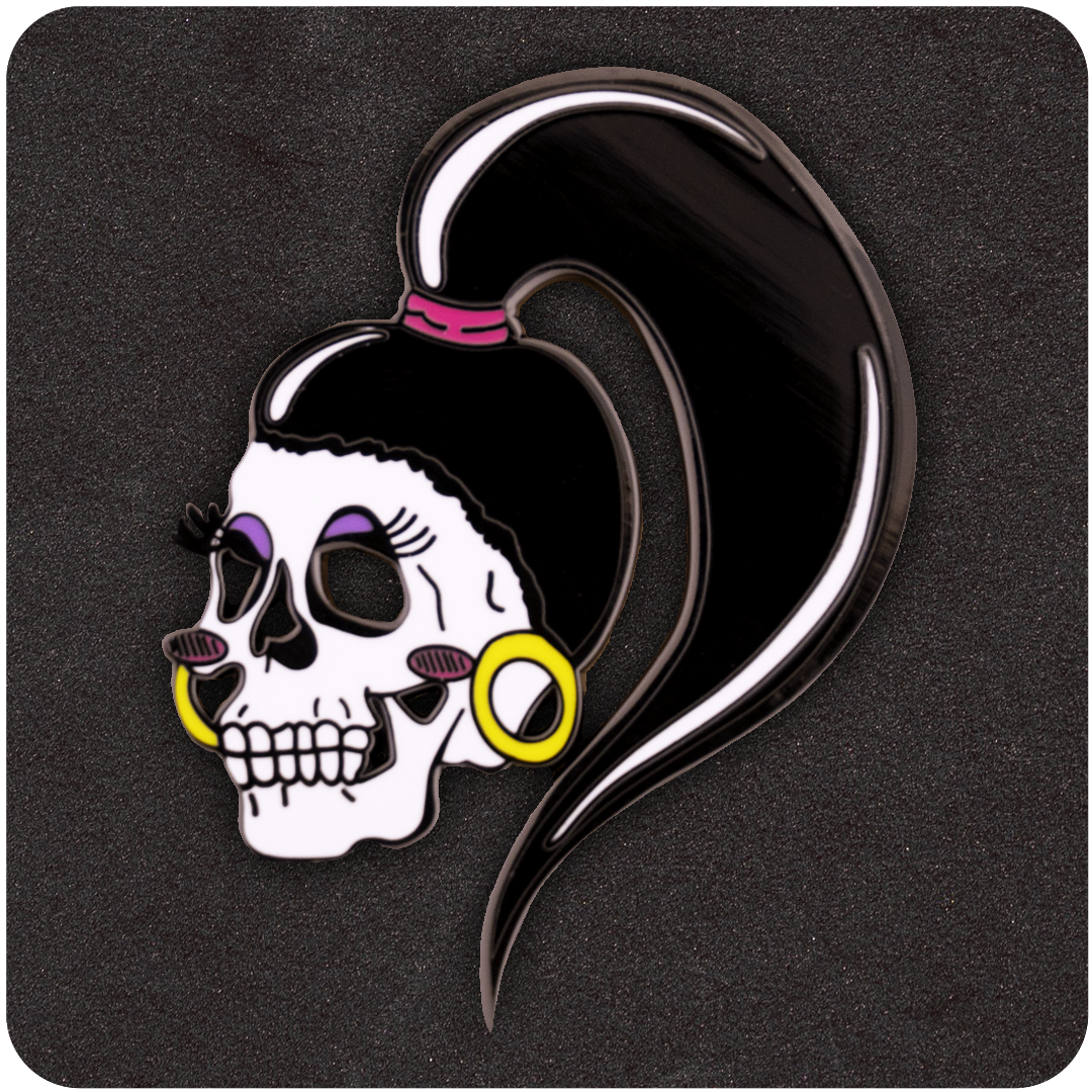 The Casual Covert Drag Me To Hell Enamel Pin. Shows a skull black enamel pin with eyeshadow. earrings, blush, and a pony tail.