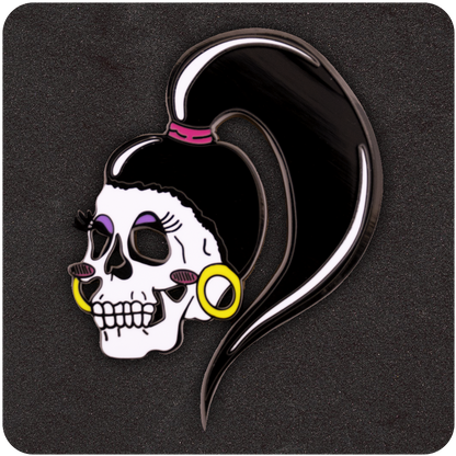 Drag Me To Hell enamel pin featuring a stylized skull with dramatic makeup, bold lashes, yellow hoop earrings, and a high ponytail on a black foam background.