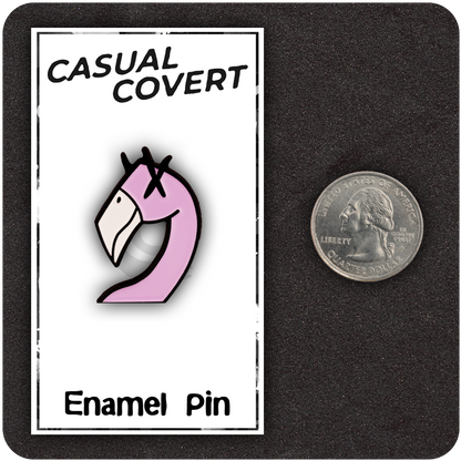 Pink flamingo enamel pin with cartoon X eyes, mounted on a white "Casual Covert" backing card labeled "Enamel Pin," shown next to a U.S. quarter for scale on a dark background.
