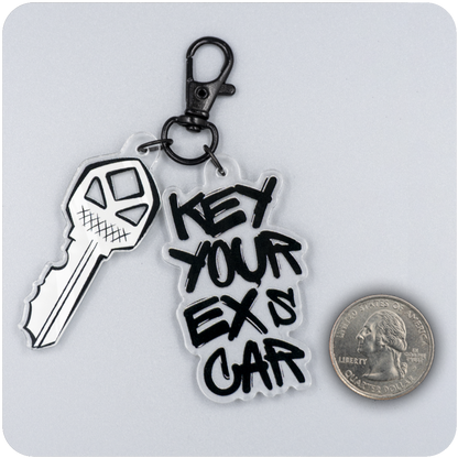 Acrylic keychain with a cartoon-style jagged key and bold black graffiti text reading “Key Your Ex’s Car,” attached to a black lobster clasp. A U.S. quarter is placed beside it on a gray background to show scale.