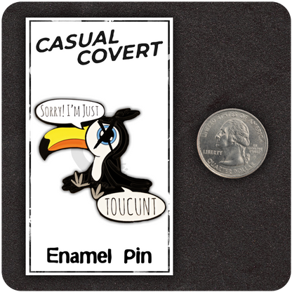 Funny enamel pin of a cartoon toucan with exaggerated features, speech bubbles reading “Sorry! I’m Just TOUCUNT,” shown next to a U.S. quarter for size reference, on a branded Casual Covert display card.
