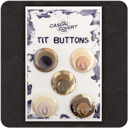 Casual Covert “Tit Buttons” pinback badge set featuring five cartoon-style nipple illustrations in diverse skin tones with playful variations, including piercings — humorous, body-positive accessory pack on branded card.