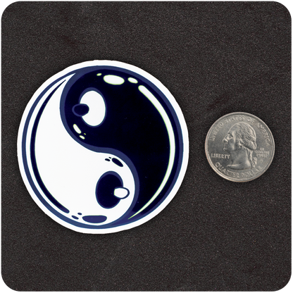 A circular sticker featuring a glossy, stylized yin-yang design with a playful twist—each of the inner dots is shaped like a cartoon nipple, giving the symbol a cheeky, breast-like appearance. The sticker is placed on a black textured background next to a U.S. quarter for scale.